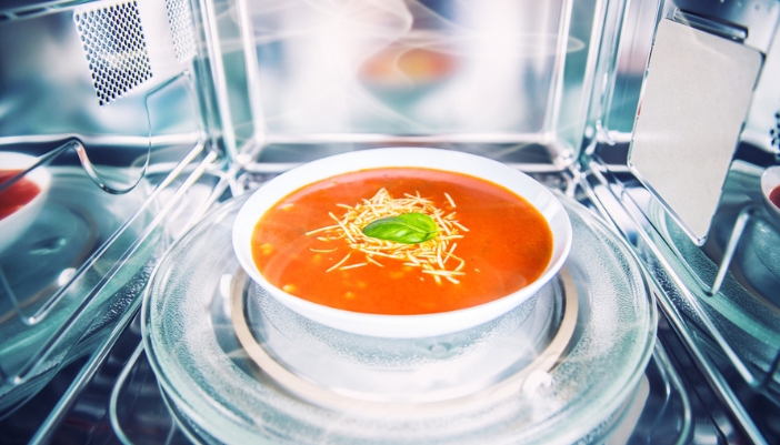 A bowl of a tomato-based soup in a microwave.