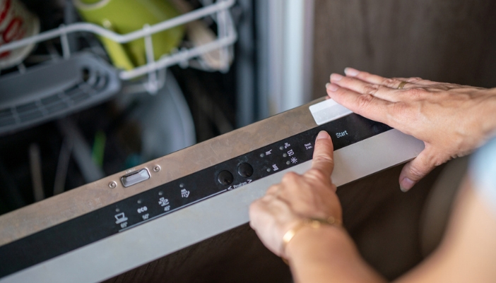 A hand chooses wash cycles on their dishwasher.