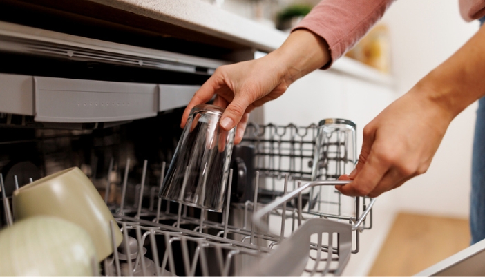 A woman loads a half-full dishwasher.