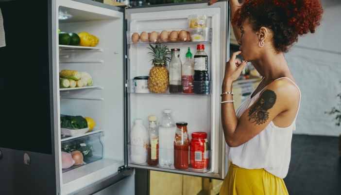 A woman looks through her open refrigerator in her kitchen.
