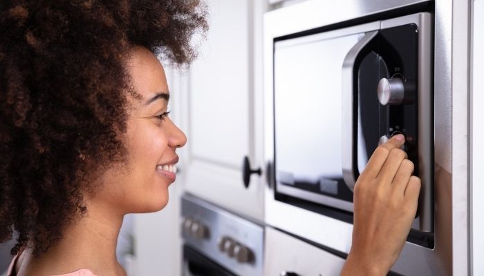 smiling young woman adjusting temperature of microwave oven 