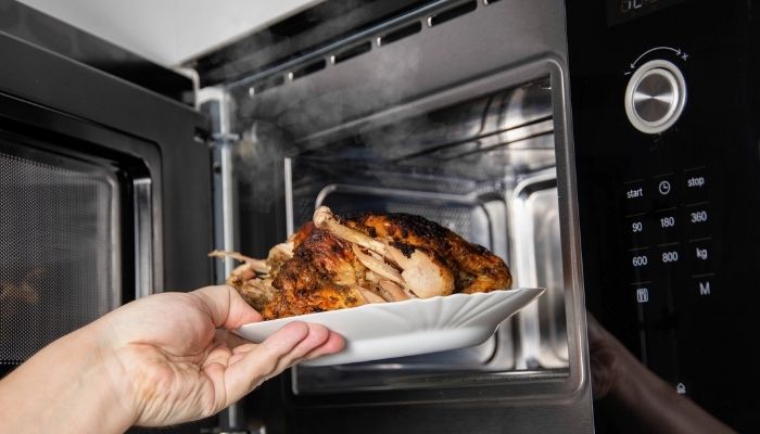 hand taking a plate of grilled chicken out of the microwave