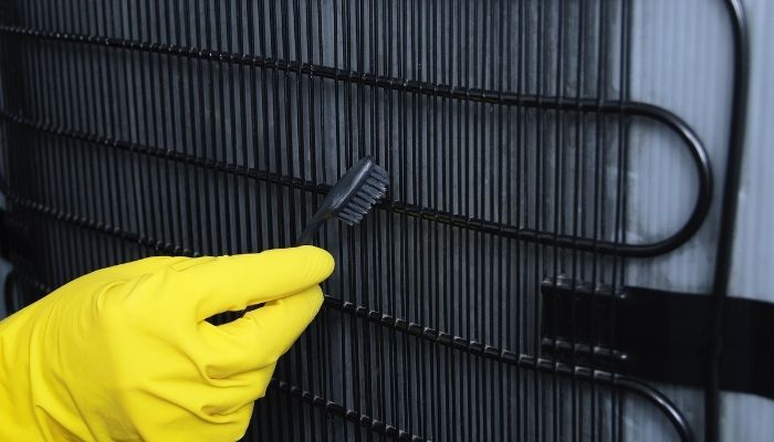 hand in a yellow glove cleans the fridge radiator grill