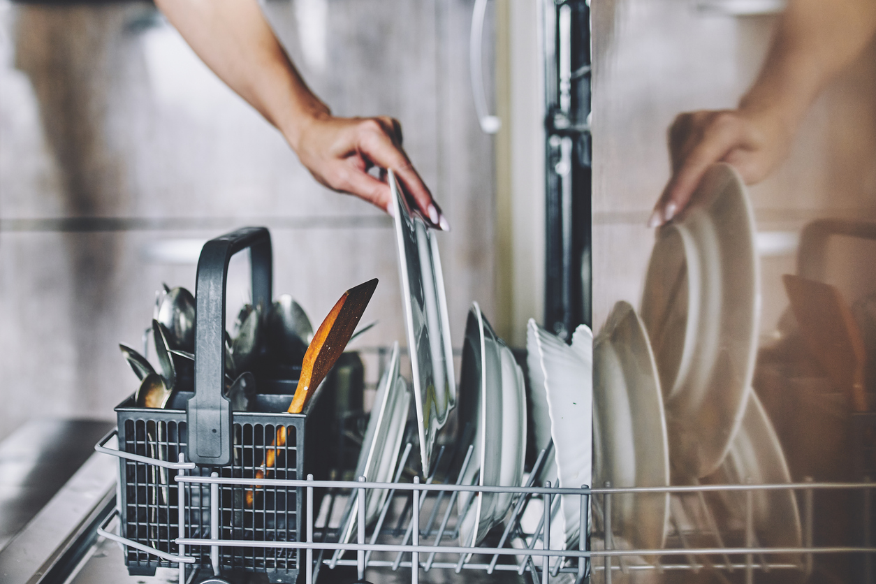 A hand reaches into a dishwasher full of clean dishes