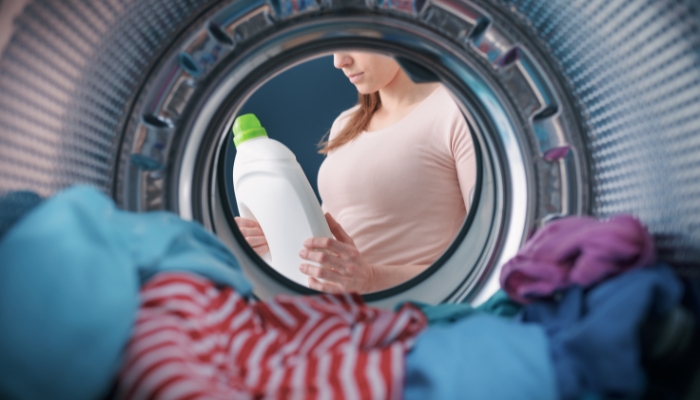 Closeup of clothes in washer machine as woman contemplates amount of detergent