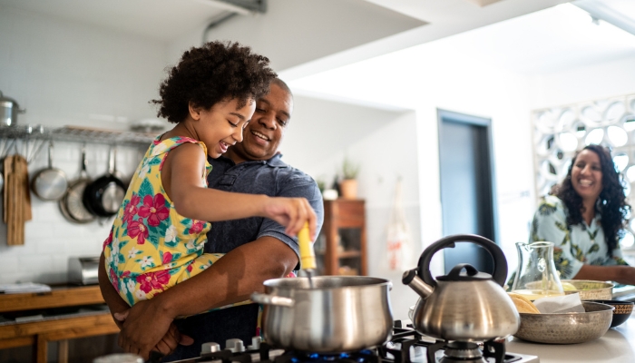 Dad helping his kid stir the pot on the cooktop
