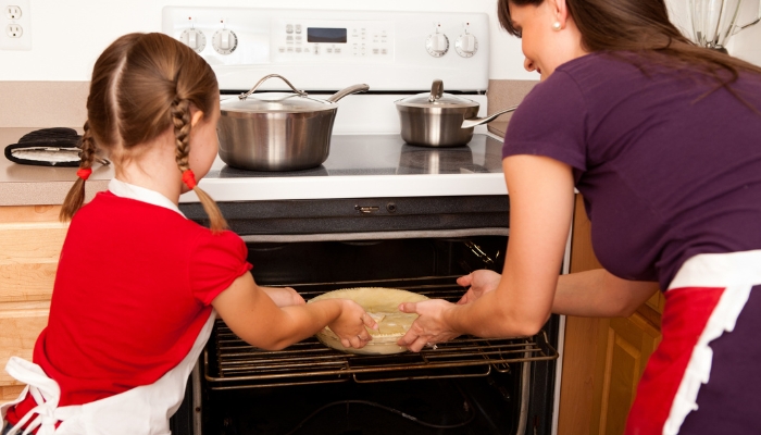 Mom and daughter putting a pie in the oven on the range, with pots on cooktop
