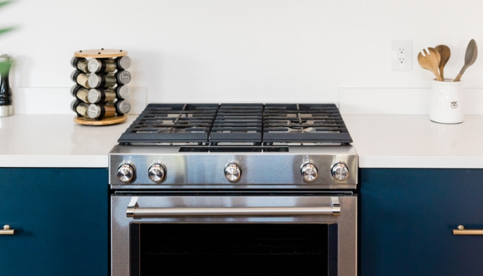 A gas range sits in a blue cabinet in front of a white wall