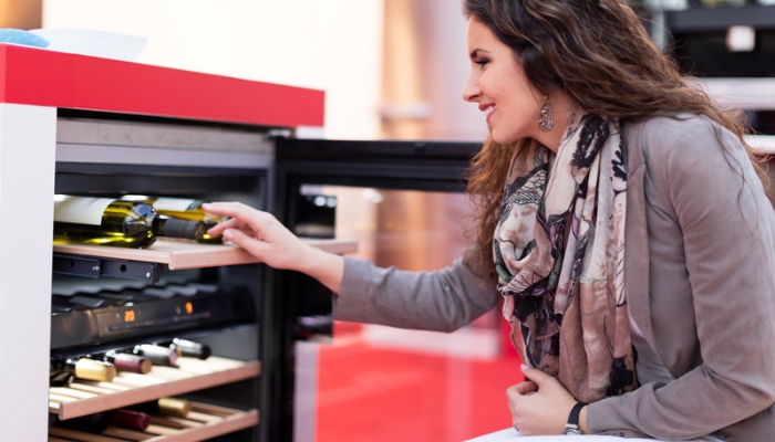 A smiling woman examines a full wine fridge in an appliance store