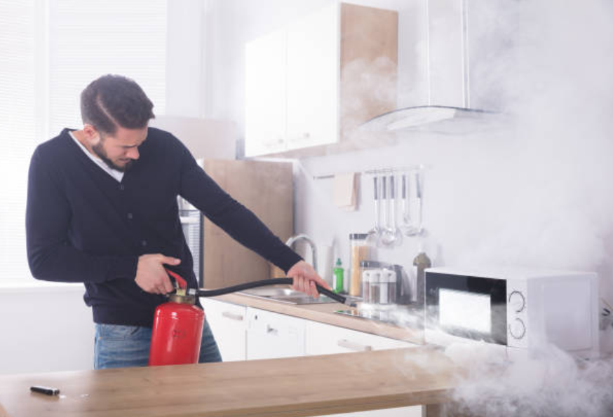 man putting out electrical fire from microwave in white kitchen