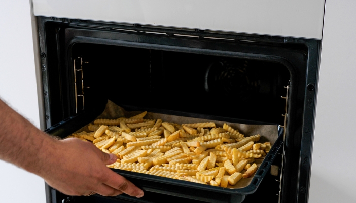 Closeup of someone putting fries to air fry in oven