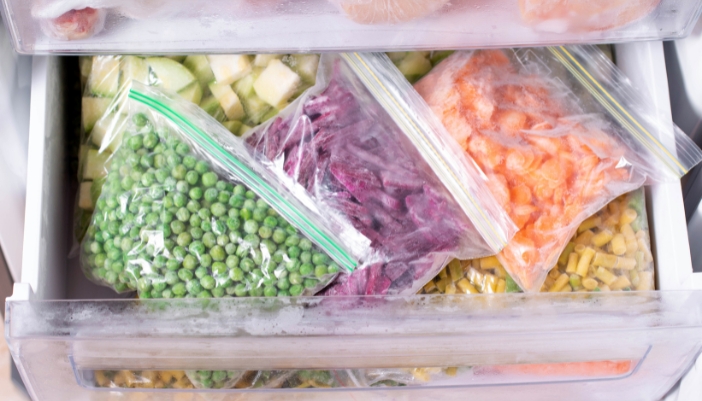 Ziploc bags of vegetables and fruit rest in an open freezer drawer.