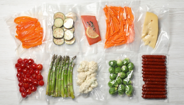 Two rows of vacuum sealed vegetables and meat on a white counter.