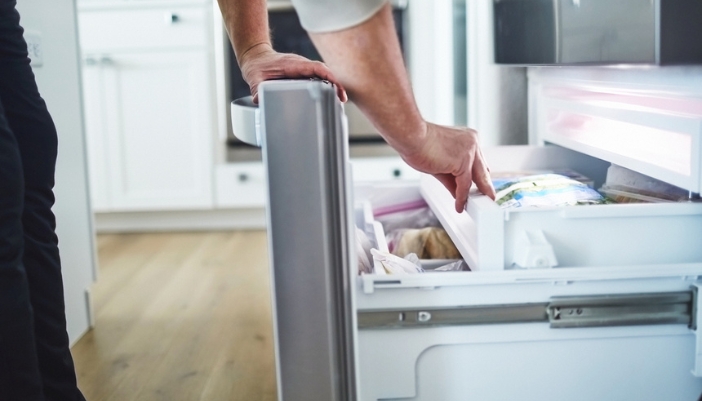 A pair of hands reach into a bottom, pull-out freezer.