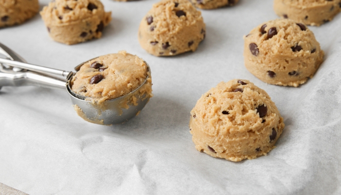 An ice cream scoop places chocolate cookie balls onto a parchment paper covered pan