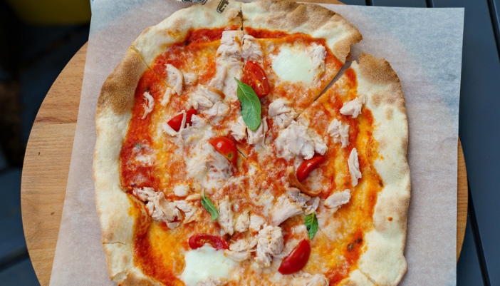 A homemade pizza rests on a wooden pan and parchment paper.