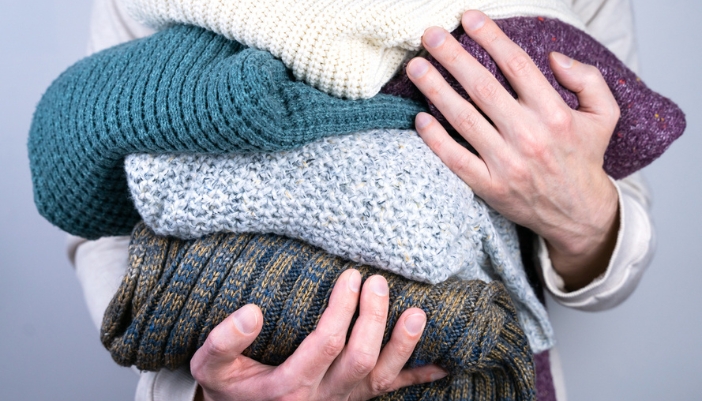 A man’s hands hold a pile of knit sweaters and cardigans.