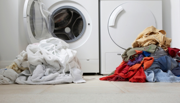 Two piles of laundry sit in front of a washer.