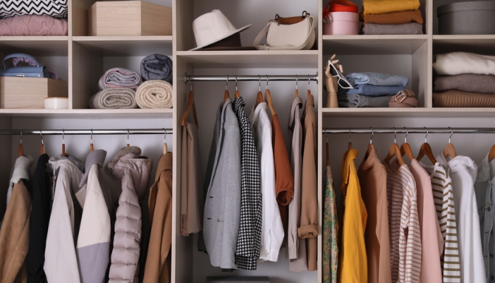 Neutral colored clothing hands in a multi-level closet.