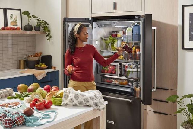 front view of a woman putting groceries into an opened french door refrigerator in a modern kitchen