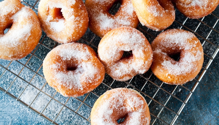 A tray of fried doughnuts sprinkled with powdered doughnuts on a cooling rack.