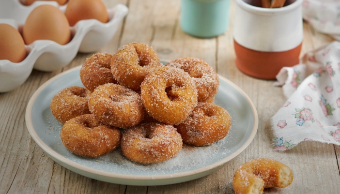 A plate of mini baked doughnuts surrounded by doughnut ingredients. 
