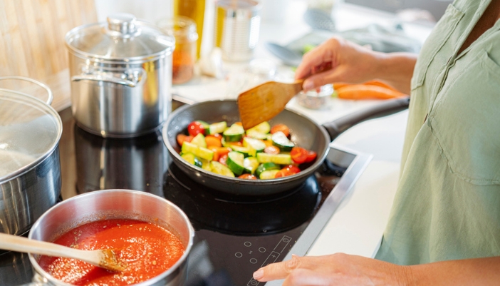 A pair of hands stirs sauce and veggies on an induction cooktop.
