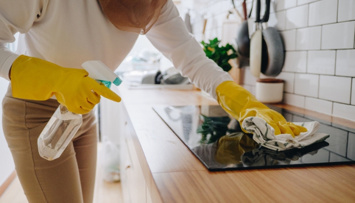 A woman wearing gloves wipes down an induction cooktop.