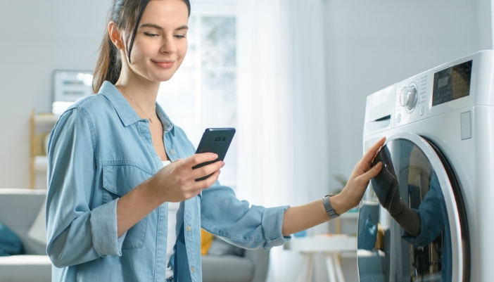 A woman uses her cell phone to set her washing machine.