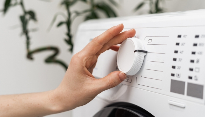 A hand turns the dial on a laundry machine to select settings.