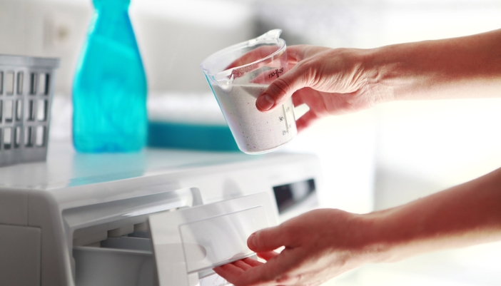 A hand fills a detergent dispenser with power detergent.