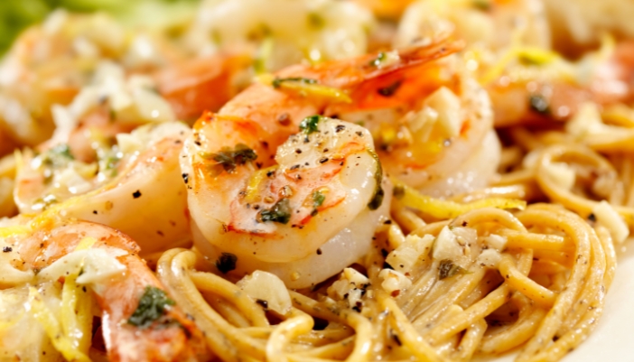 A close-up of garlic shrimp over a bed of pasta.