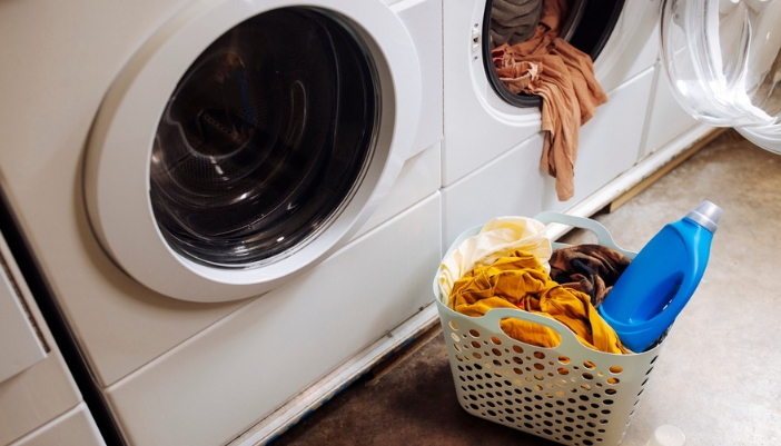 An open washing machine with an overflowing basket and bottle of detergent.