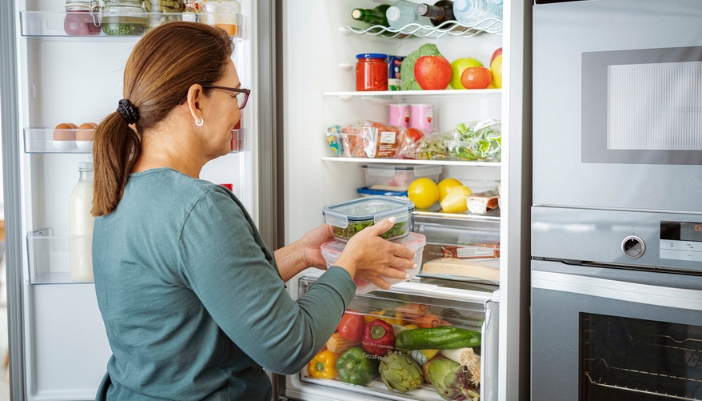 A woman tries to put leftovers into her very full fridge.