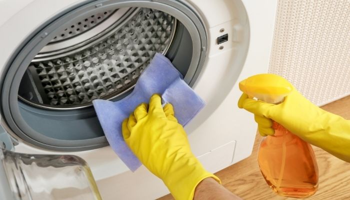 Someone spraying and wiping down front load washer
