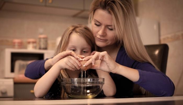 Mom helping daughter to crack an egg