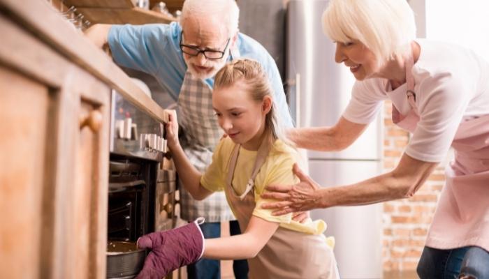 Grandparents helping teen put dish in oven
