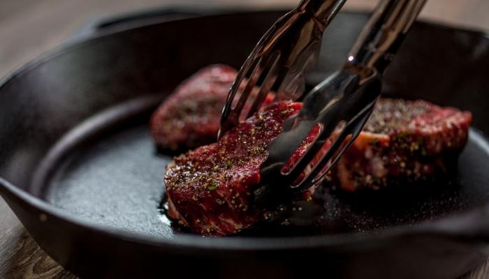 steaks being placed in a cast-iron