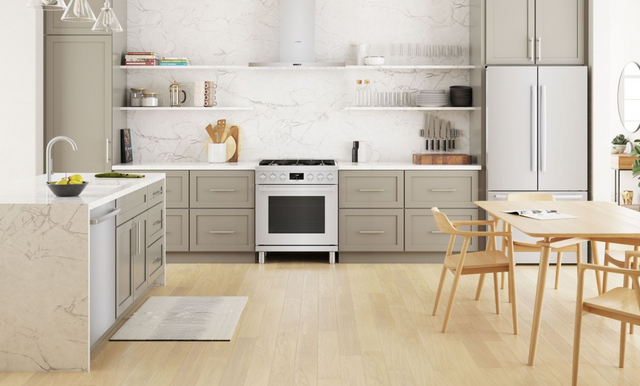 front view of a modern kitchen with beige light wood floors and beige cabinets, and centered in the cabinetry is a 30" gas range