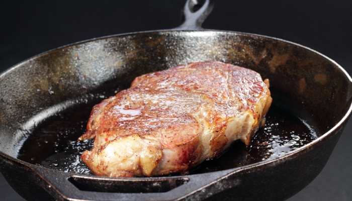 A steak cooks in a cast iron pan with oil