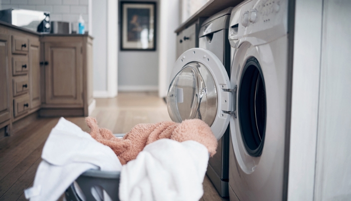 A basket of laundry sits in front of an open dryer.