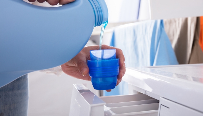 A woman’s hands pours laundry detergent into the washer.