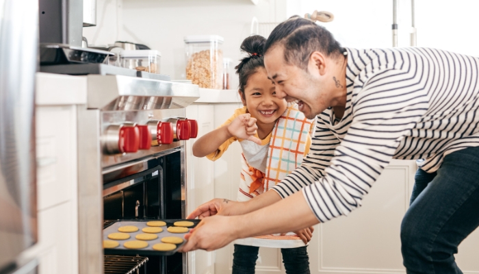 A happy man and a child pull a pan of sugar cookies out of an oven.