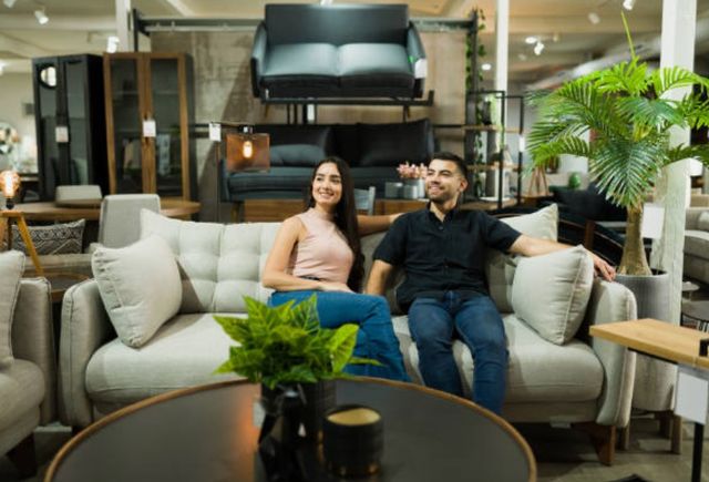 front view of a man and woman sitting and smiling on a beige sofa in a furniture store