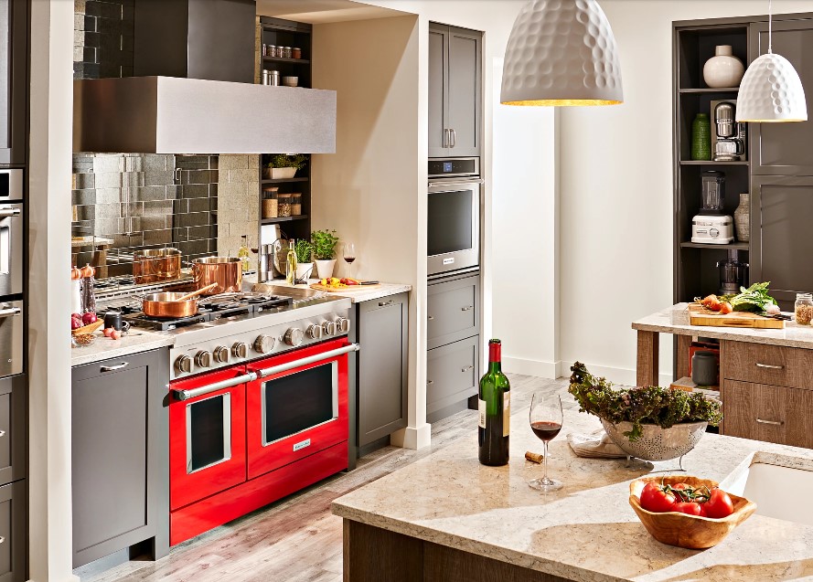 luxury kitchen with wolf appliances, copper cookware on the stove, white overhead lighting hanging from the ceiling, and a glass of wine on the countertop.