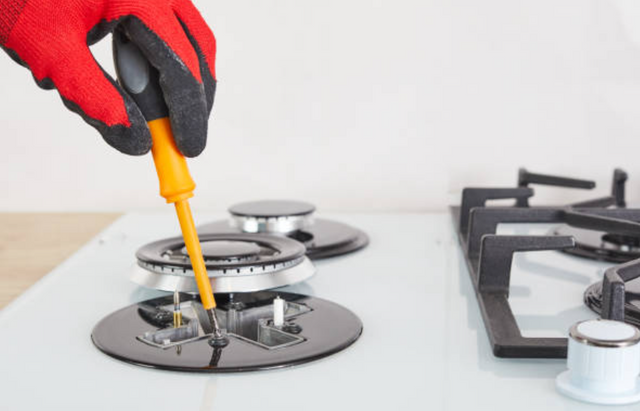 front view of a hand wearing a red glove screwing in the burners on a white gas rangetop