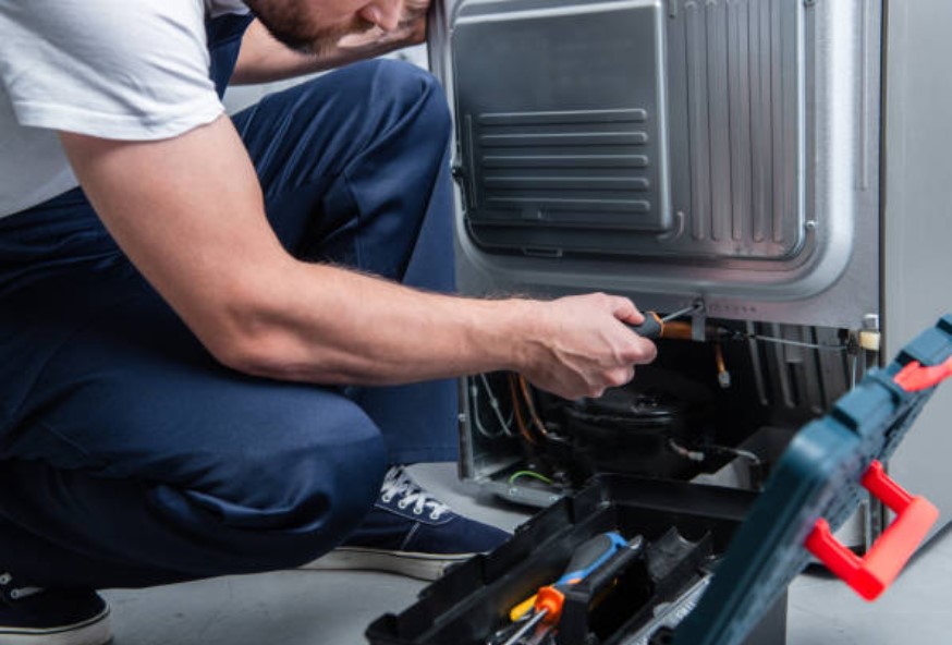 man kneeled with toolbox fixing the bottom of a refrigerator