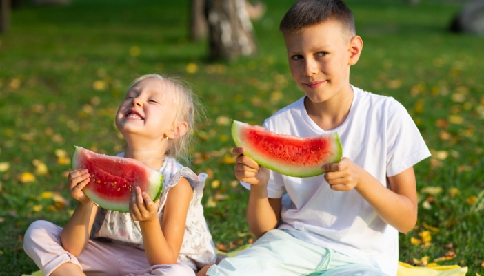 Two kids munching on watermelon in the park