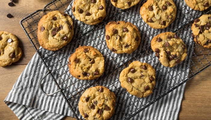 Freshly baked, gooey chocolate chip cookies rest on a cooling rack above a towel.