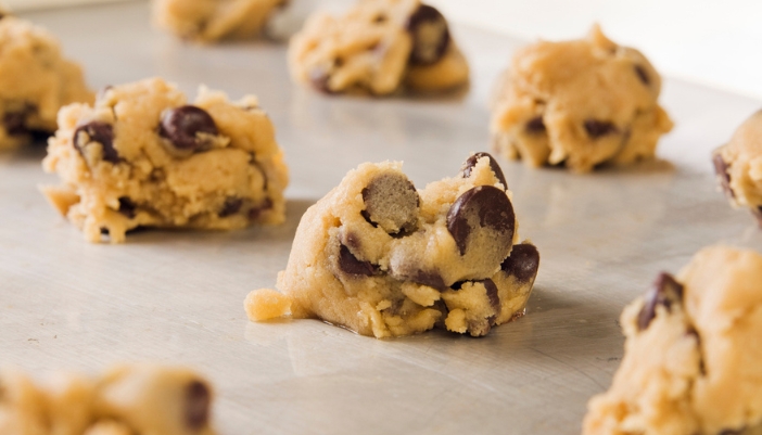 Balls of uncooked chocolate chip cookie dough on a baking sheet.